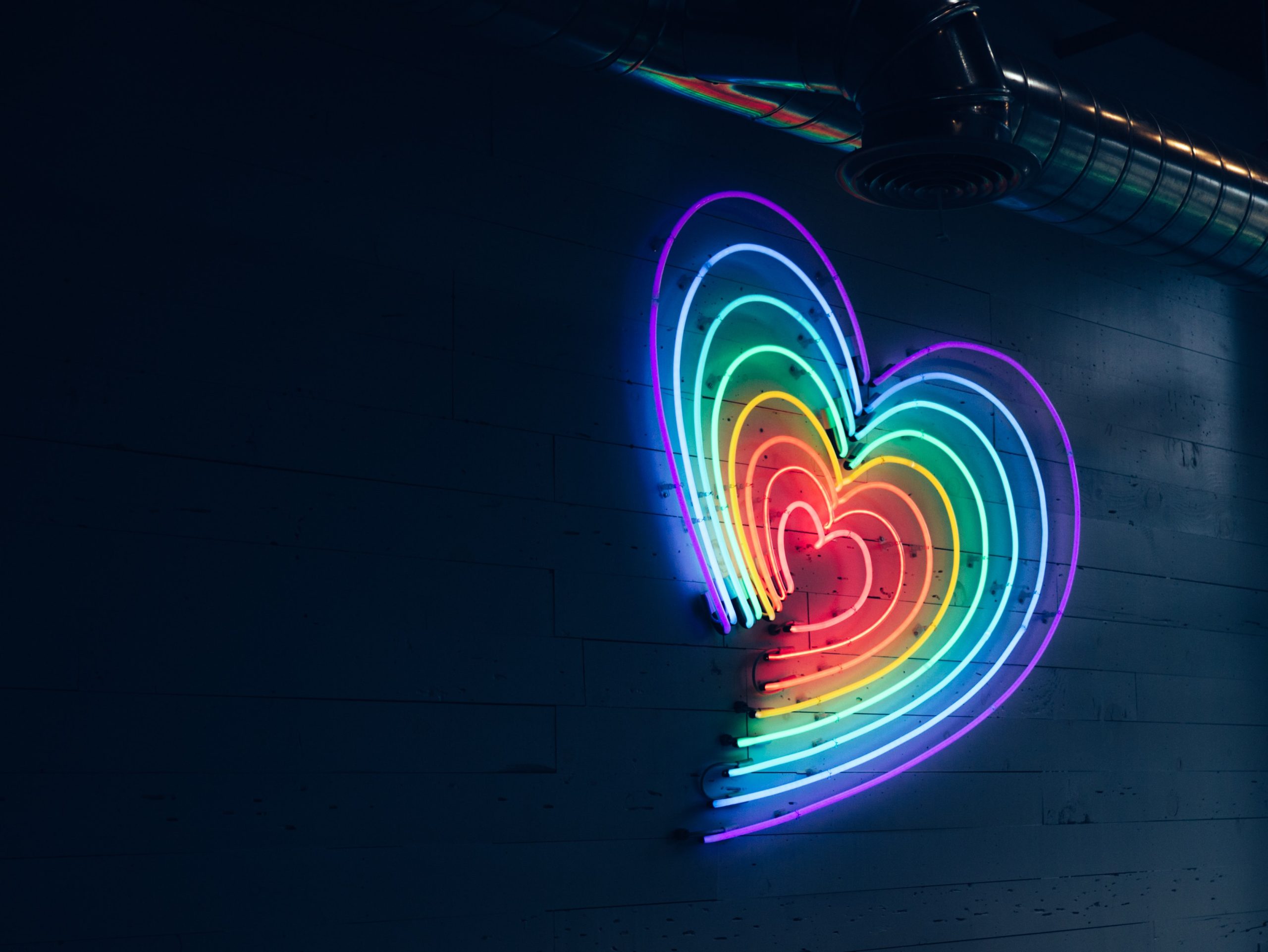 ein regenbogenfarbenes Neon-Herz vor dunklem Hintergrund