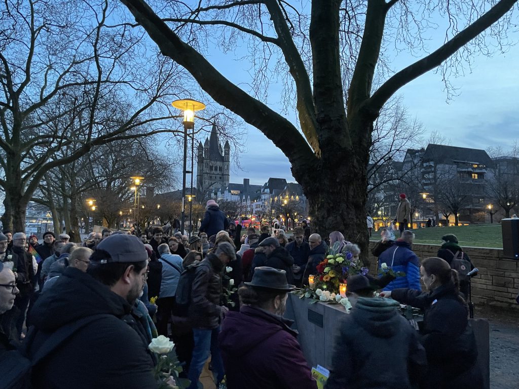 Eine Gruppe von Menschen versammelte sich in der Abenddämmerung um einen Baum und würdigte feierlich die queeren Opfer und Gedenken des Holocaust.