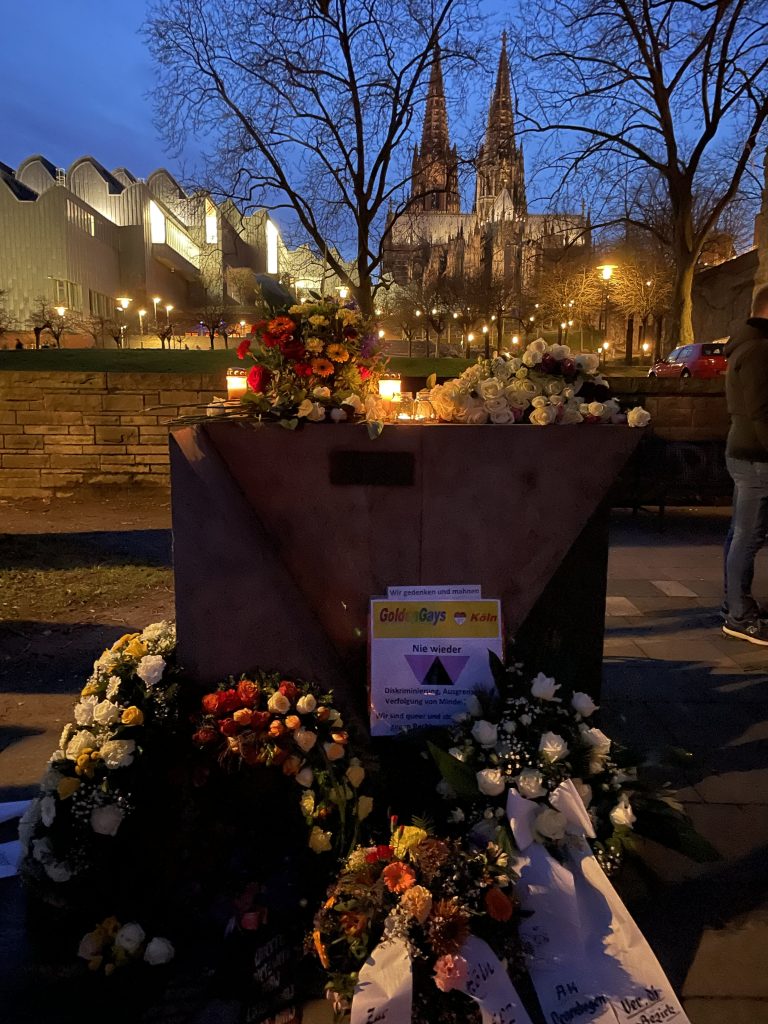Blumen von Queeren Opfern werden vor einem Dom in Köln niedergelegt.